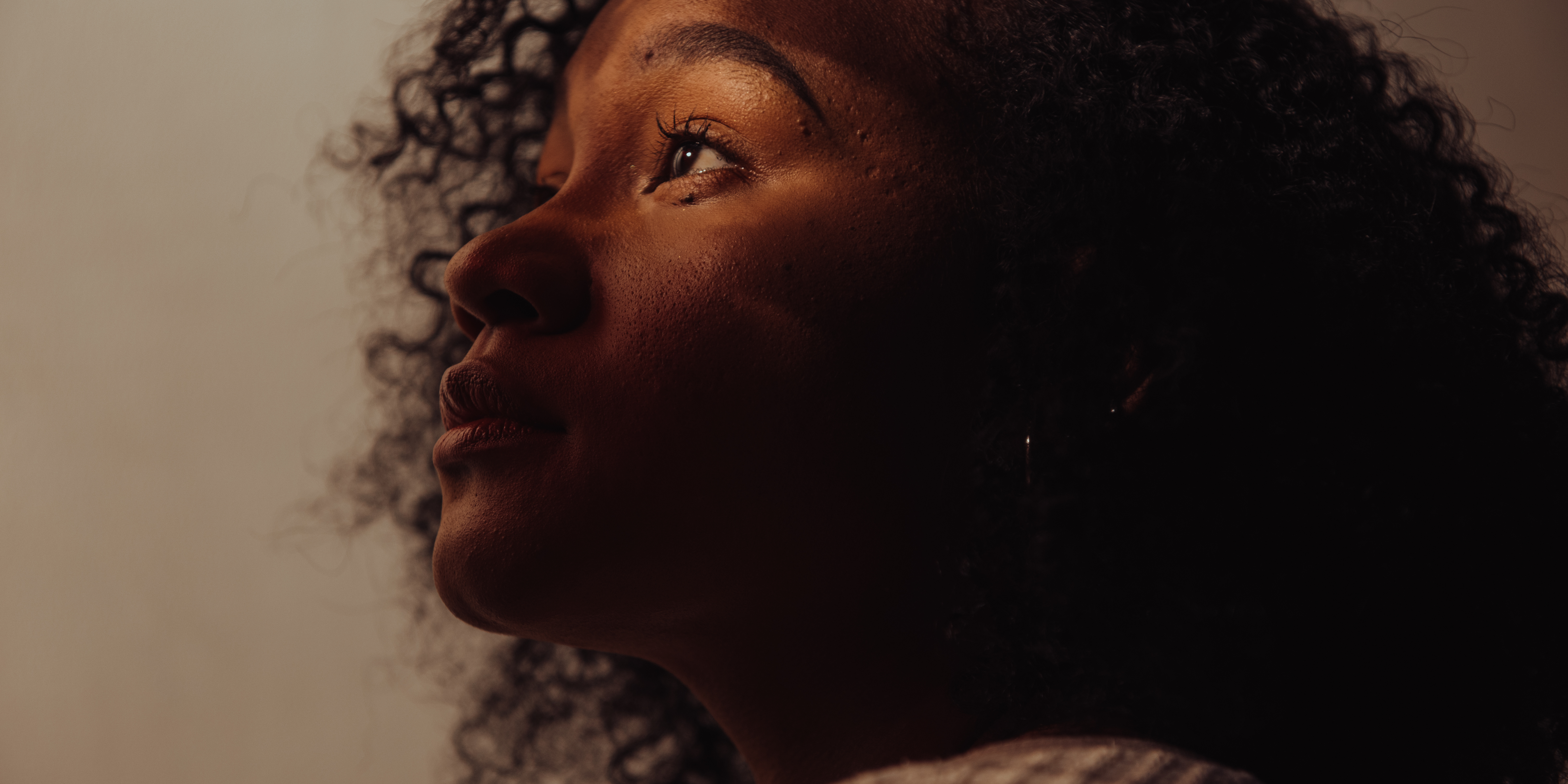 Woman of colour gazing upwards with a contemplative expression, shadow across her face